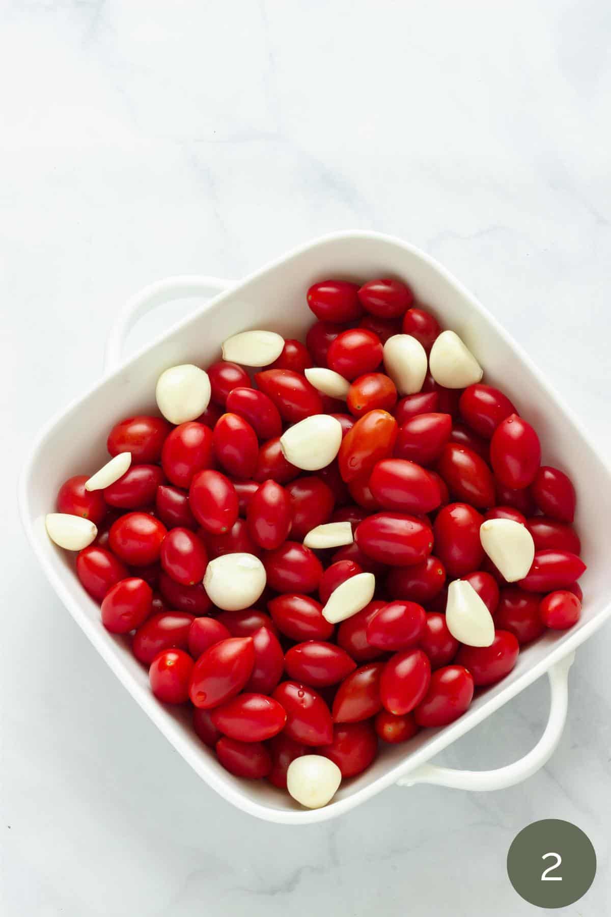 A baking dish full of grape tomatoes and garlic cloves.