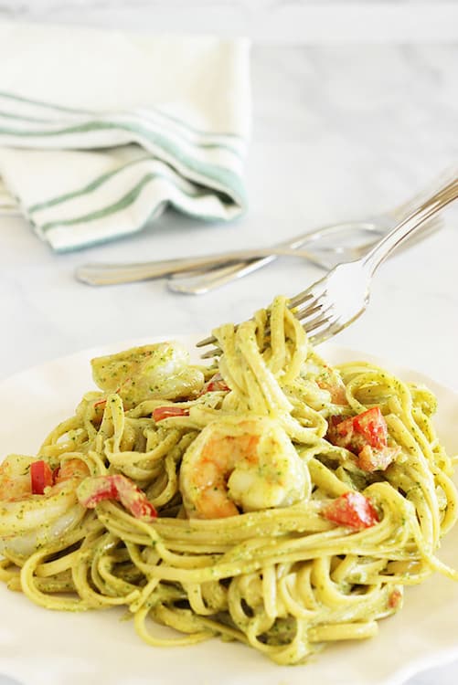 A fork lifting pasta from a plate of Fettuccine and Shrimp with Arugula Pesto Cream Sauce. 