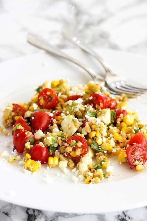 A plate of summer freekeh salad with grilled corn, tomatoes, cilantro, roasted chiles, and fresh mozzarella.