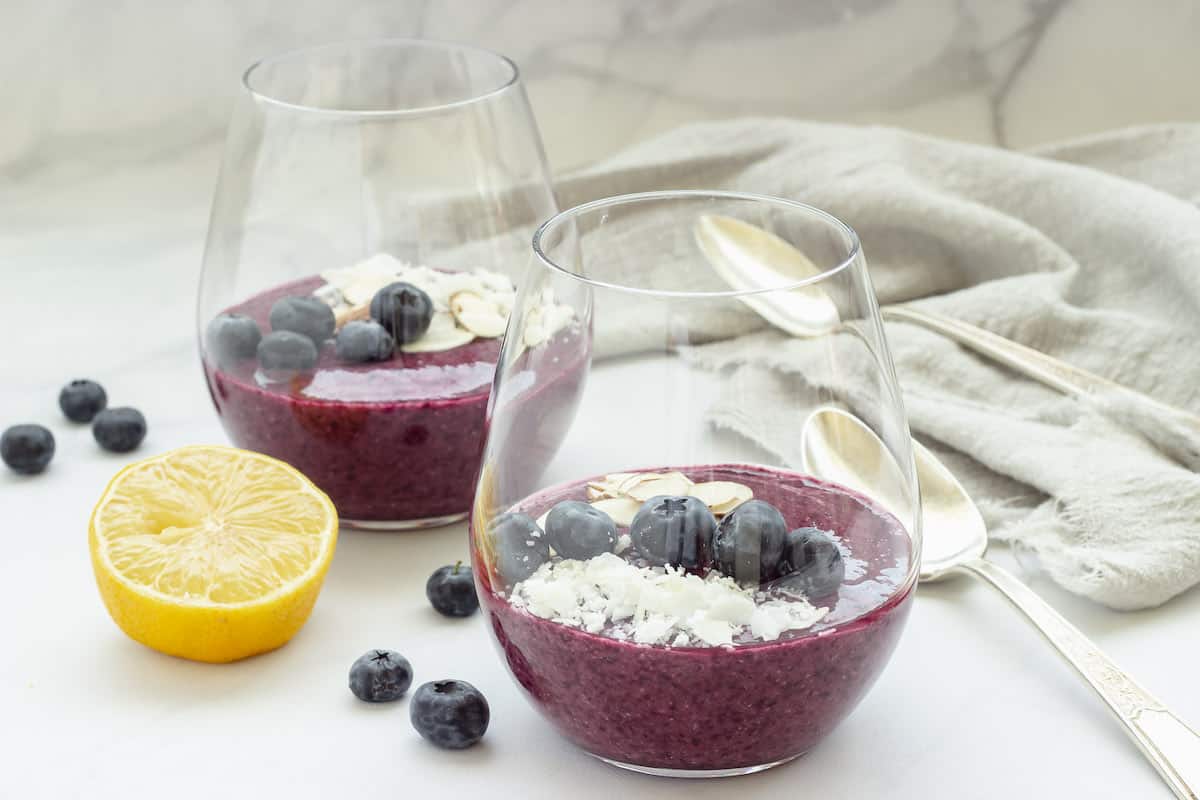 2 glasses with blueberry chia pudding garnished with coconut, fresh blueberries, and sliced almonds. 