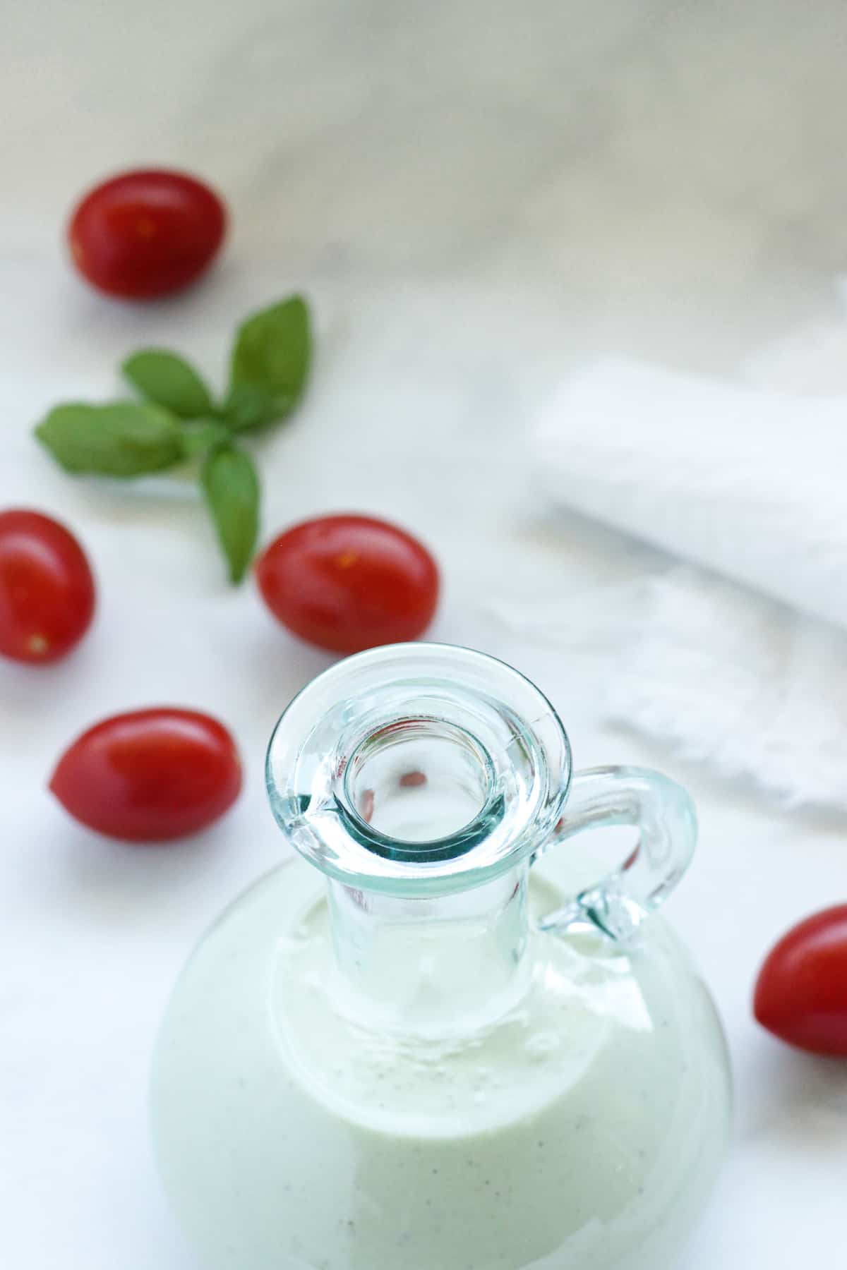 overhead shot of a bottle of homemade blue cheese vinaigrette salad dressing surrounded by cherry tomatoes and a sprig of basil