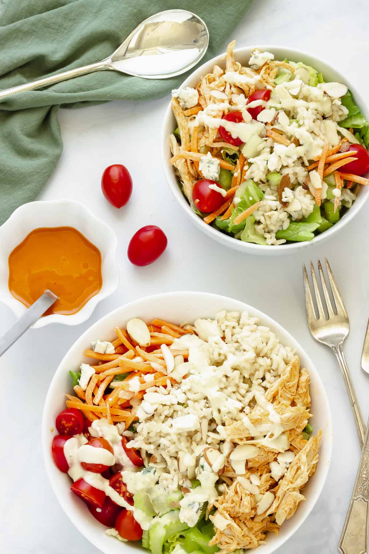 2 buffalo chicken rice bowls with a small bowl of buffalo sauce and grape tomatoes in the background.