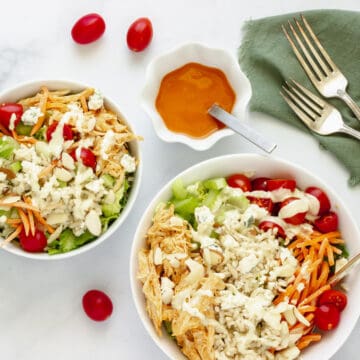 2 buffalo chicken rice bowls with a small bowl of buffalo sauce and grape tomatoes in the background.