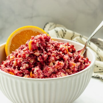 A white bowl of low sugar cranberry orange relish with an orange slice and spoon.