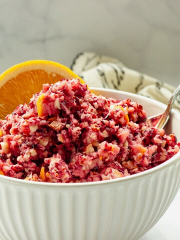 A white bowl of low sugar cranberry orange relish with an orange slice and spoon.