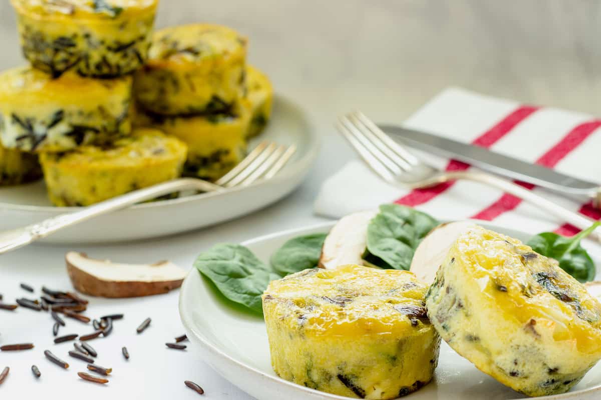 A plate with 2 egg muffin cups in the foreground and a platter of egg muffin cups in the background.