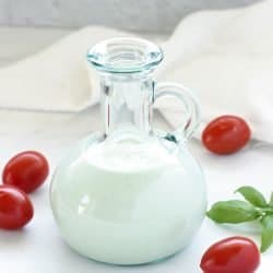 Salad dressing bottle with homemade blue cheese dressing surrounded by grape tomatoes and basil