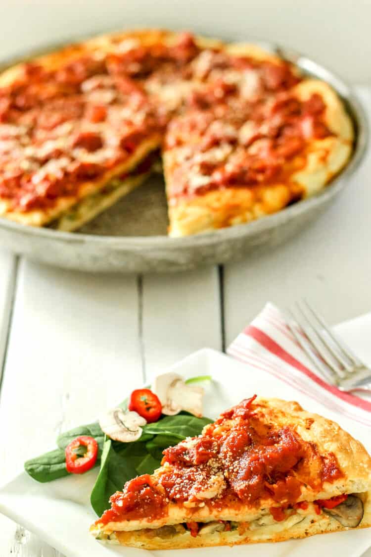 A slice of Chicago-style stuffed pizza with a pan of pizza in the background