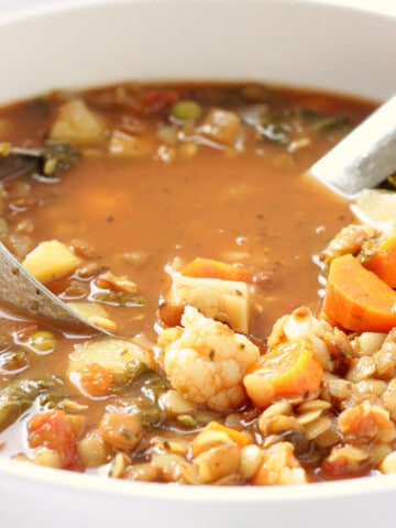 A white soup pot of heart healthy mediterranean vegetable lentil soup with a ladle.