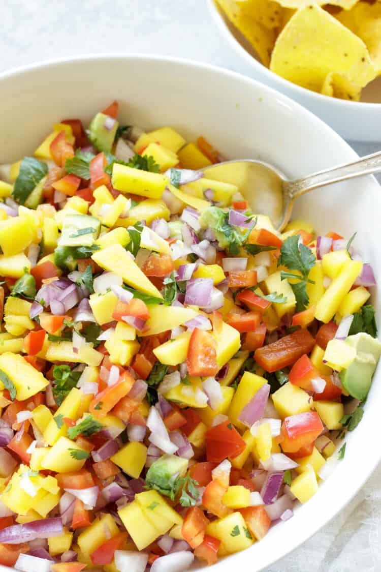 A white bowl of colorful mango habanero salsa and a small bowl of tortilla chips next to it.