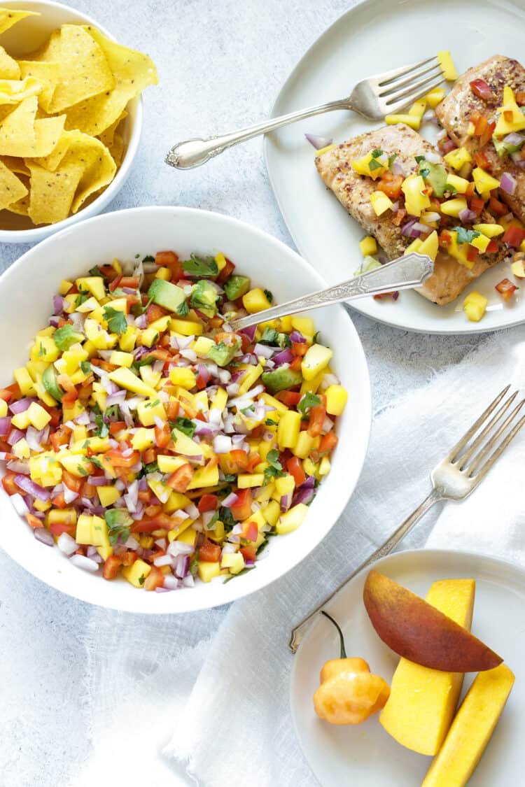 large bowl of Mango Habanero Salsa with a bowl of tortilla chips and a plate of salmon topped with mango salsa.