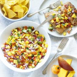 A large bowl of mango habanero salsa with a bowl of chips and a plate of salmon topped with mango salsa