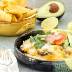 A casserole dish with Green Chicken Enchilada Pie a bowl of tortilla chips, half and avocado and lime in the background