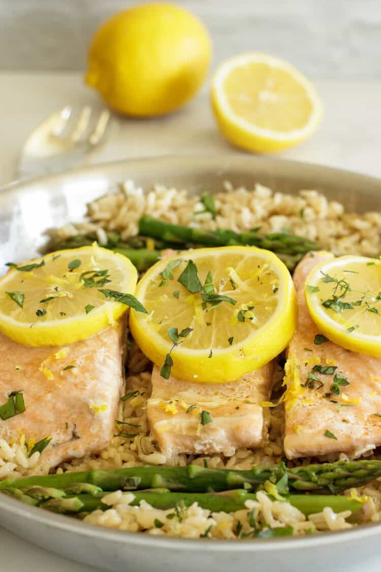 three pieces of salmon with lemon slices on top of brown rice with asparagus