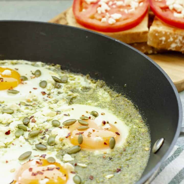 A skillet with Pesto Eggs. Bread and tomatoes are in the background.