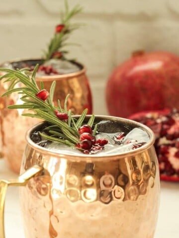 2 copper mugs with pomegranate mule cocktails garnished with a rosemary sprig and pomegranate arils
