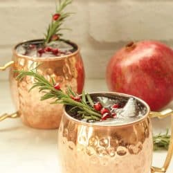2 copper mugs with pomegranate mule drinks garnished with rosemary sprig and pomegranate arils