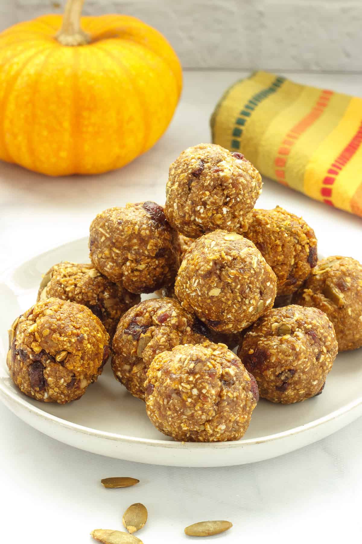 A plate of pumpkin spice protein balls. A small pumpkin and striped napkin are in the background.