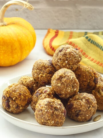 A plate of pumpkin spice protein balls with a small pumpkin and a striped napkin in the background.