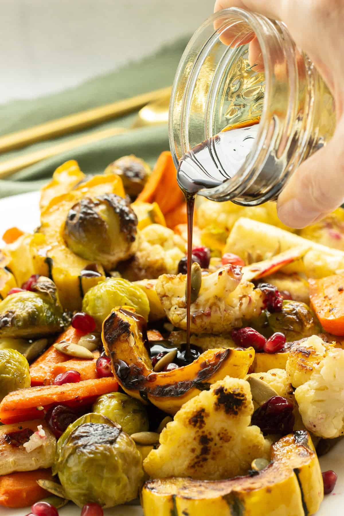 A jar of balsamic glaze being poured over a platter of roasted fall vegetables
