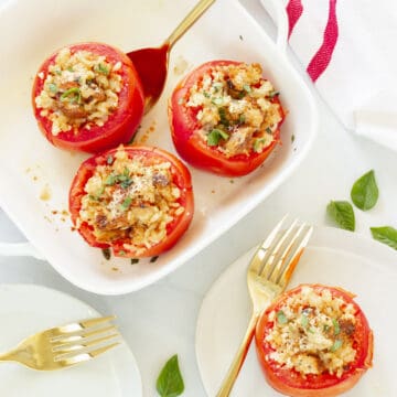 A white casserole dish with baked stuffed tomatoes. One tomato is on a plate in the background