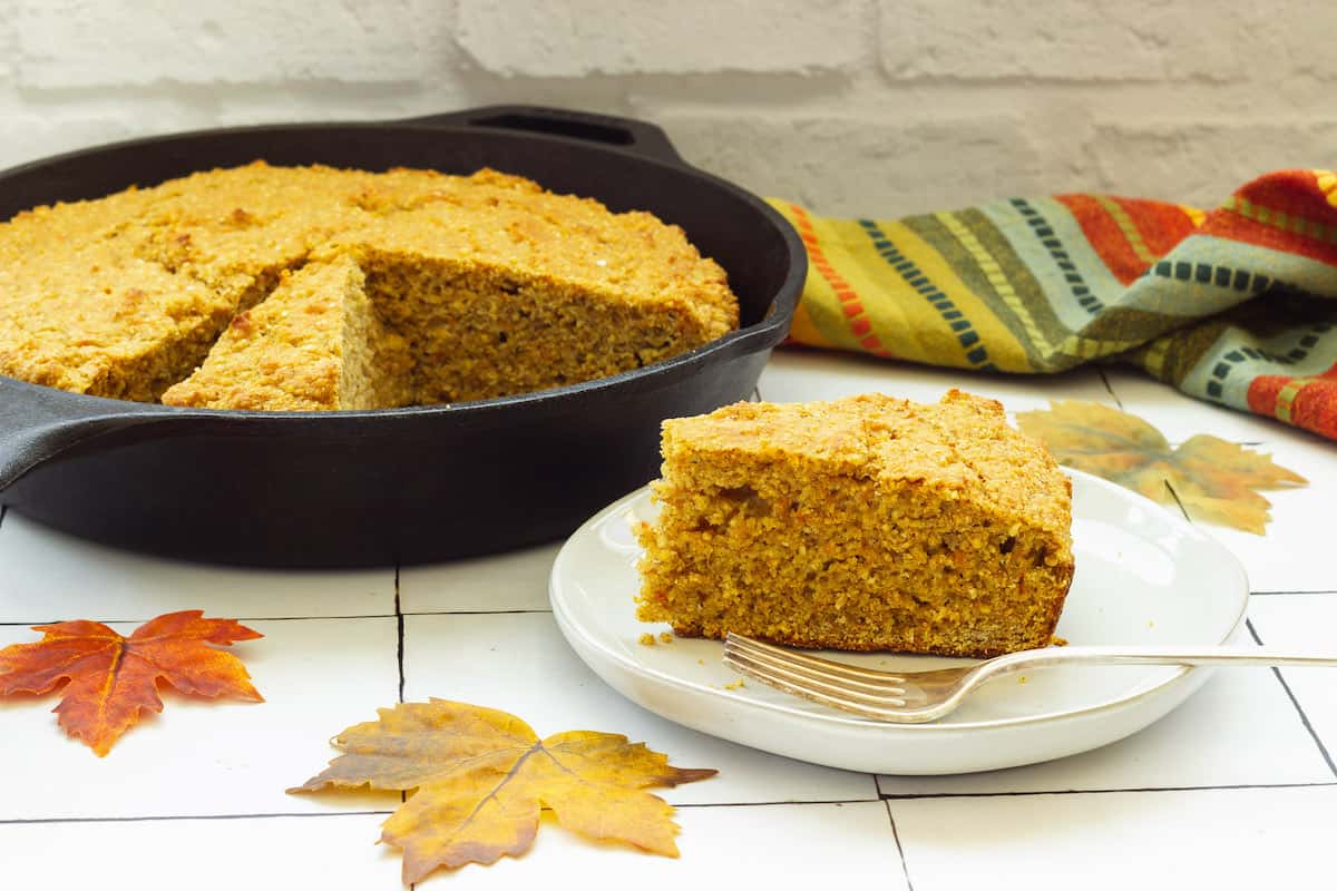 A wedge slice of sweet potato cornbread. A skillet with cornbread is in the background.