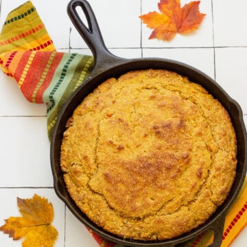 A cast iron skillet with sweet potato cornbread. A fall napkin and fall leaves are in the background.