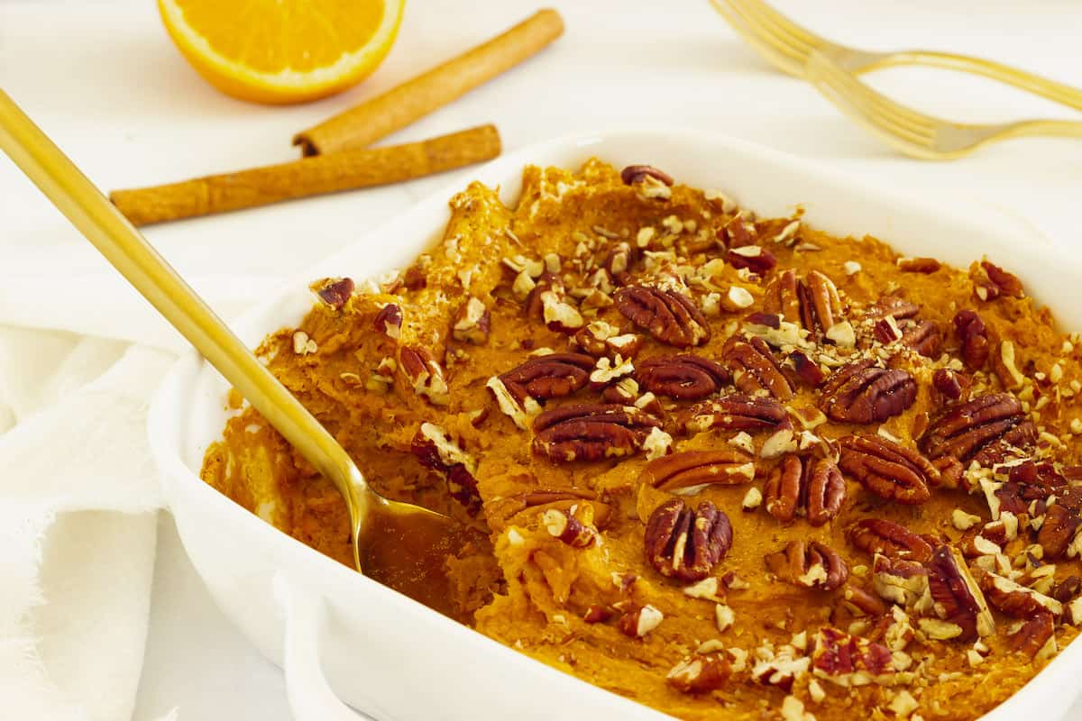 A white casserole dish with sweet potato souffle and a gold serving spoon.