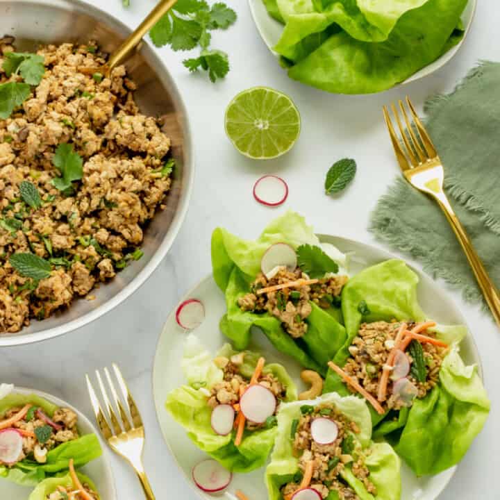 A white plate with tofu lettuce wraps. A skillet with the scrambled tofu filling, a bowl of lettuce leaves, and a lime half are in the background.