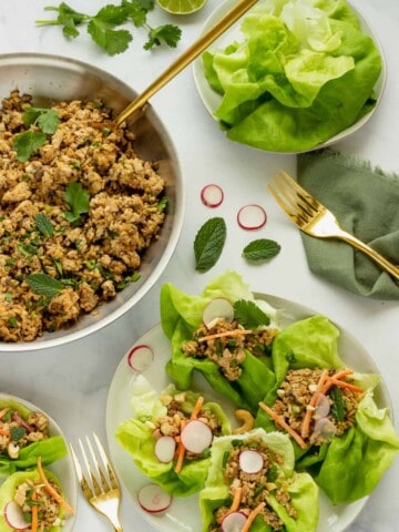 A white plate with tofu lettuce wraps. A skillet of the ground tofu filling and a bowl of lettuce leaves are in the background.